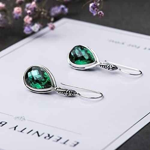 Elegant silver earrings with green gemstones on a decorative paper.