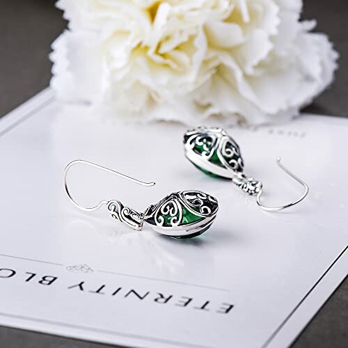 Elegant silver and green earrings on floral background.